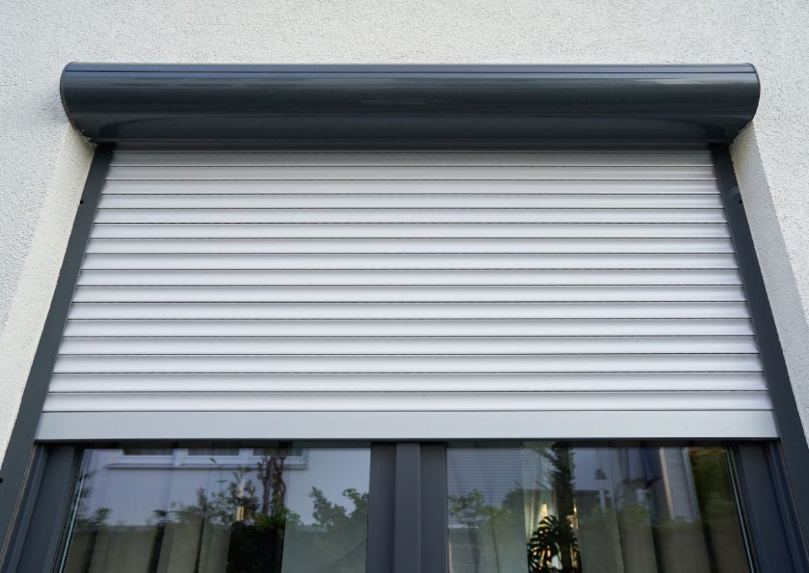 Volet roulant extérieur moderne de couleur gris clair, partiellement descendu devant une fenêtre.