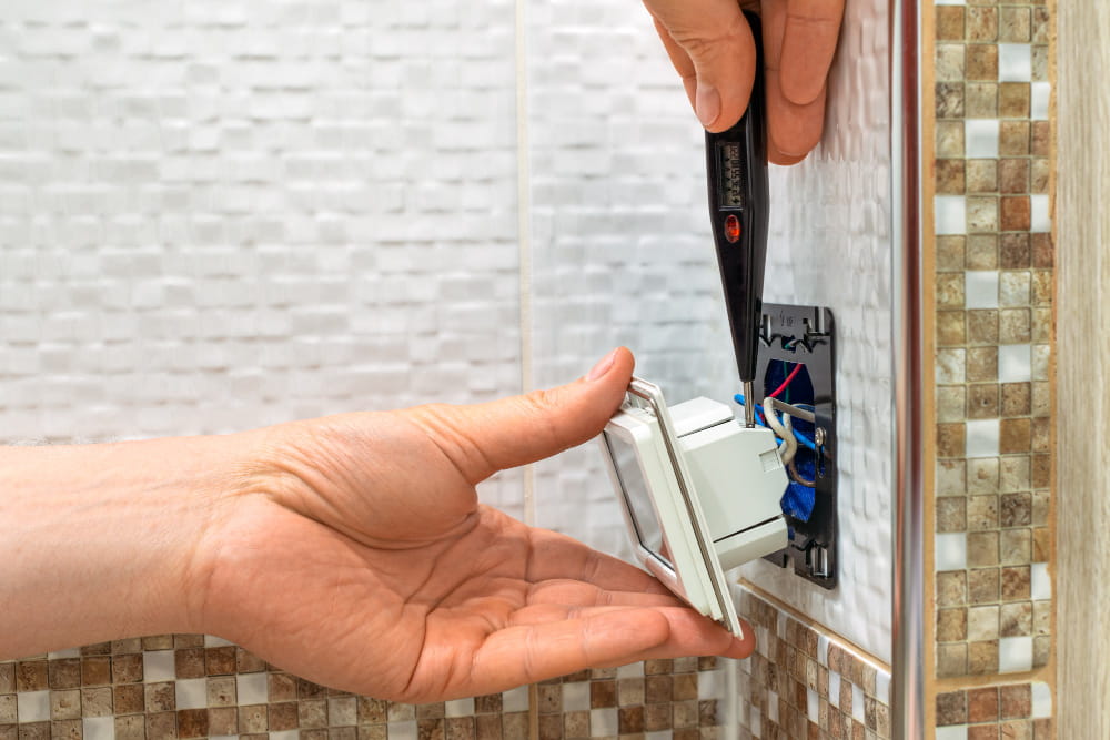 Un électricien utilisant un testeur de tension sur une prise murale pour diagnostiquer des interruptions de courant