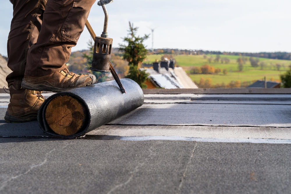 Artisan couvreur utilisant un chalumeau pour l'installation d'un revêtement bitumeux, étape clé de l'entretien toitures plates