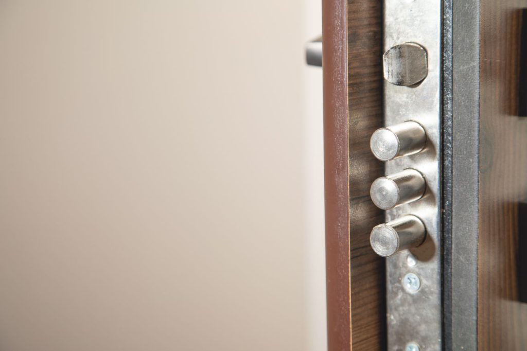 Gros plan sur les pênes d'une serrure multipoints en acier, installée sur la tranche d'une porte blindée en bois foncé, illustrant la précision technique d'une pose porte blindee sur mesure serrurier paris.